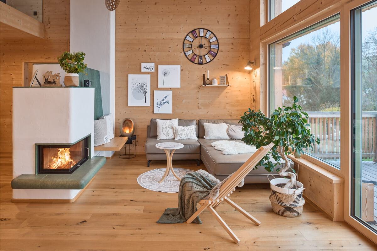 Gemütliches Wohnzimmer mit einem Kamin in einem Thoma Vollholzhaus. Der Boden sowie die Wände sind mit Holz100 Elementen gebaut. - Tipps zur Verbesserung der Wohngesundheit  - Thoma Holz100