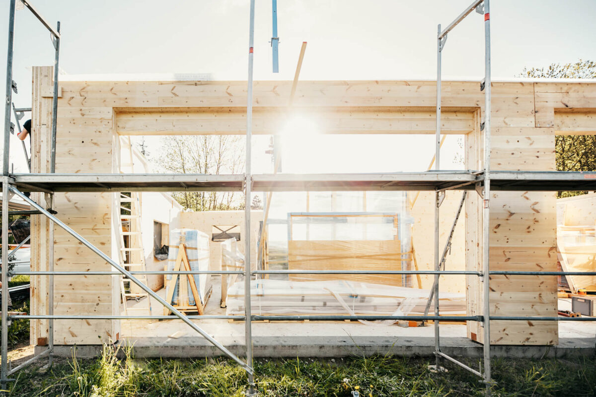 Blick auf eine Baustelle, auf der ein Vollholzhaushaus mit Holz100 Elementen errichtet wird. Das Bild wurde gegen die Sonne aufgenommen. - Veranstaltungen bei unseren Holz100 Partnern - Thoma Holz100